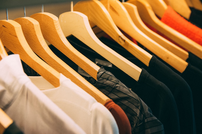 A row of wooden hangers holds a variety of clothes, dominated by white, black, and orange garments. The clothes appear to be neatly arranged in a sequence, suggesting a retail display or a well-organized closet.