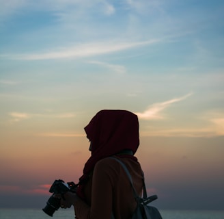 woman holding DSLR camera near body of water