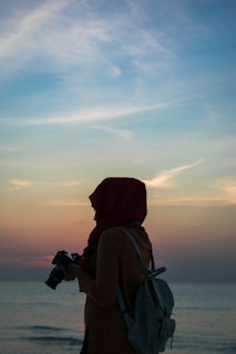 woman holding DSLR camera near body of water