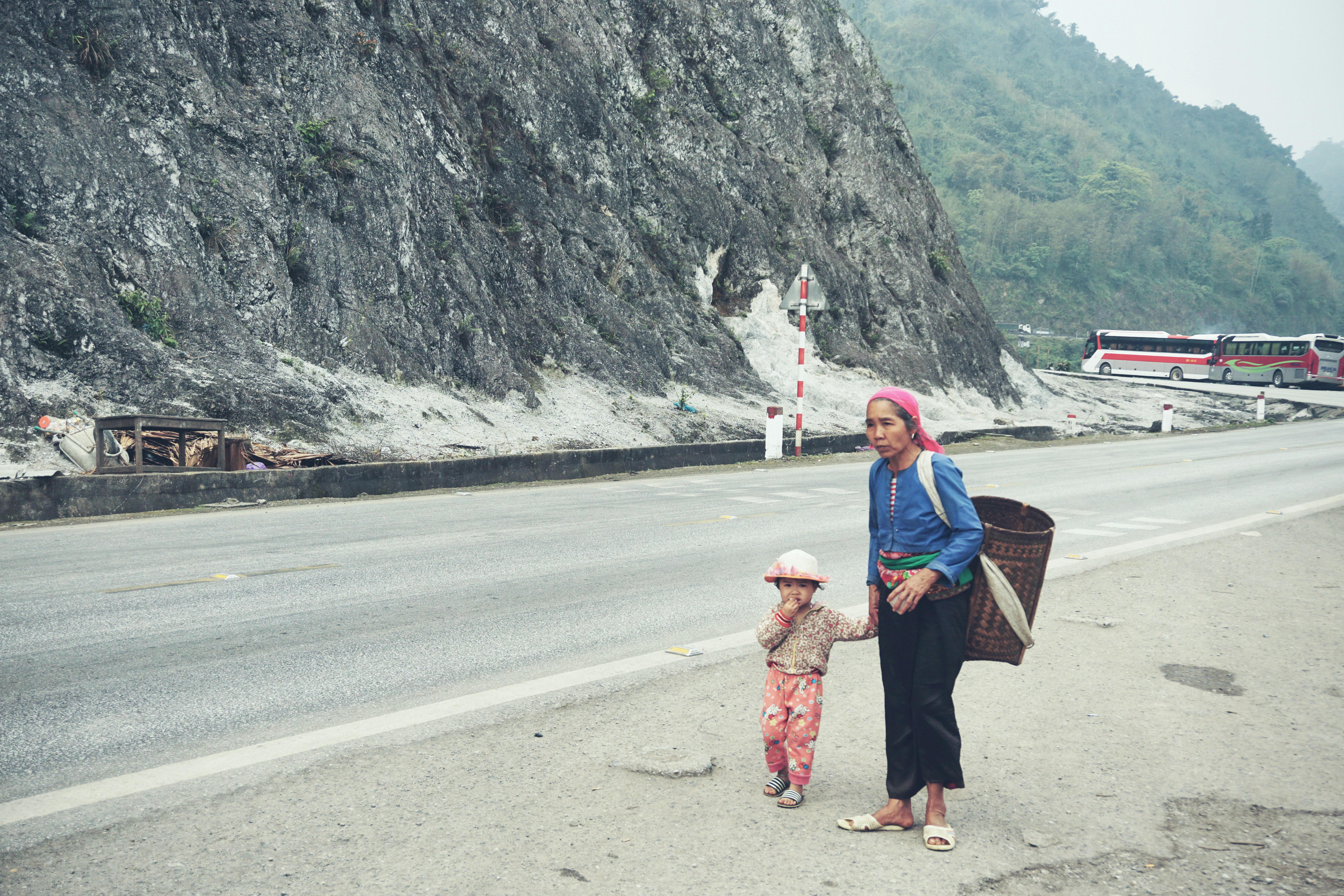 woman holding toddlers hand walking beside road