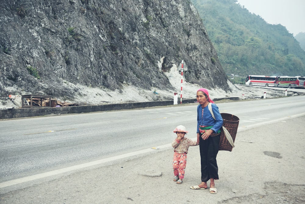 woman holding toddlers hand walking beside road