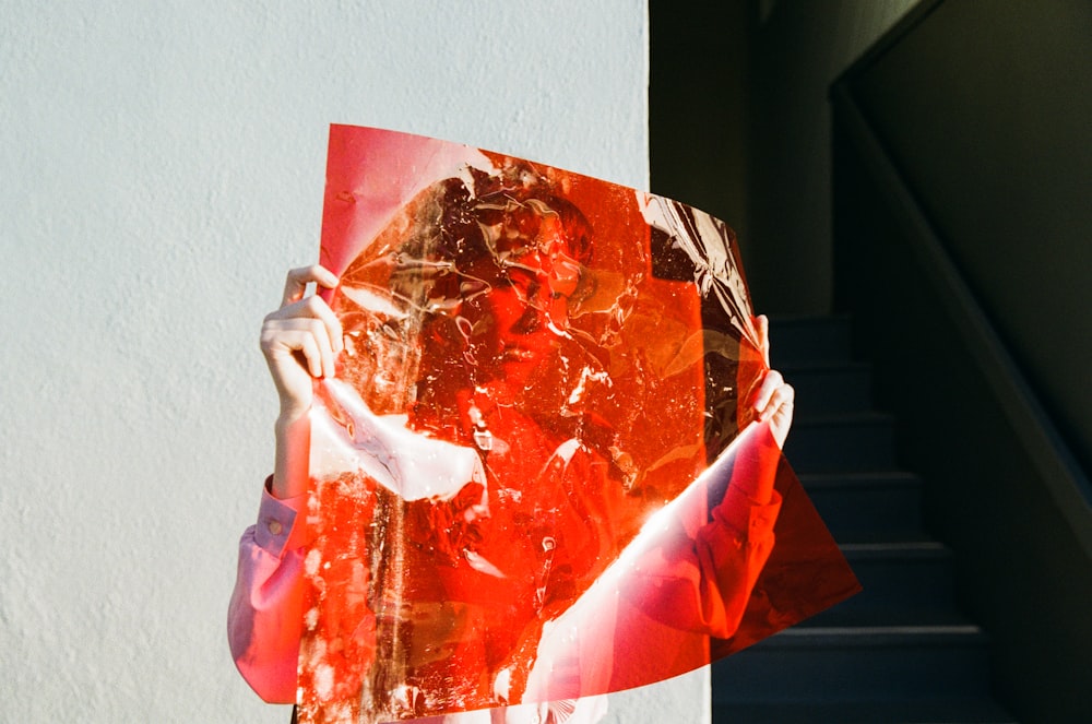 woman holding red film beside wall