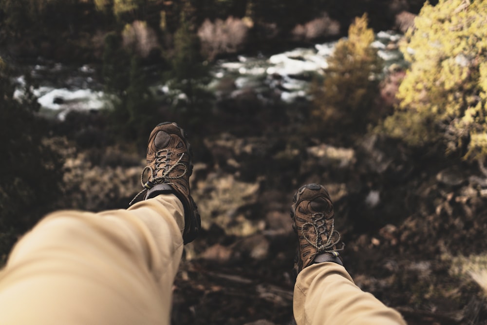 person wearing brown hiking boots sitting on cliff
