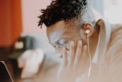 A person with headphones is sitting and appears to be focused or absorbed in what they are listening to or watching on a device. The background is slightly blurred, highlighting the person as the focal point.