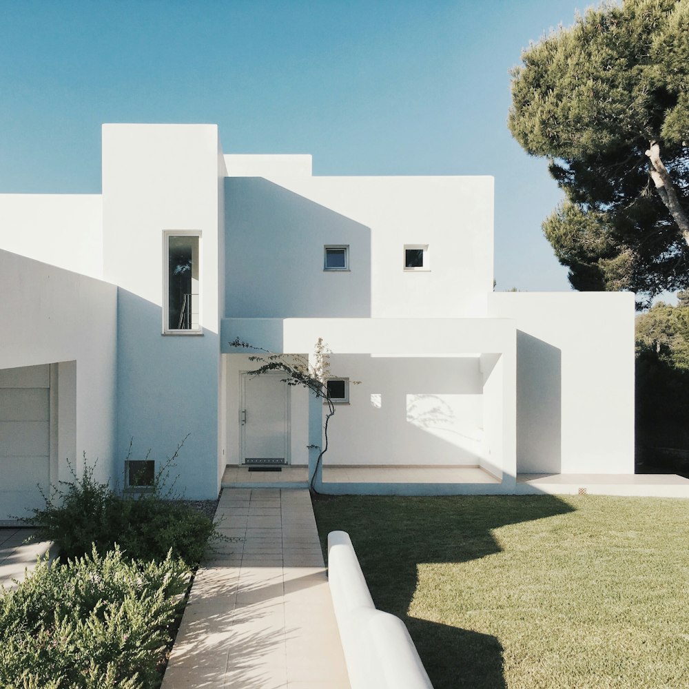 Maison en béton blanc près de l’arbre vert pendant la journée