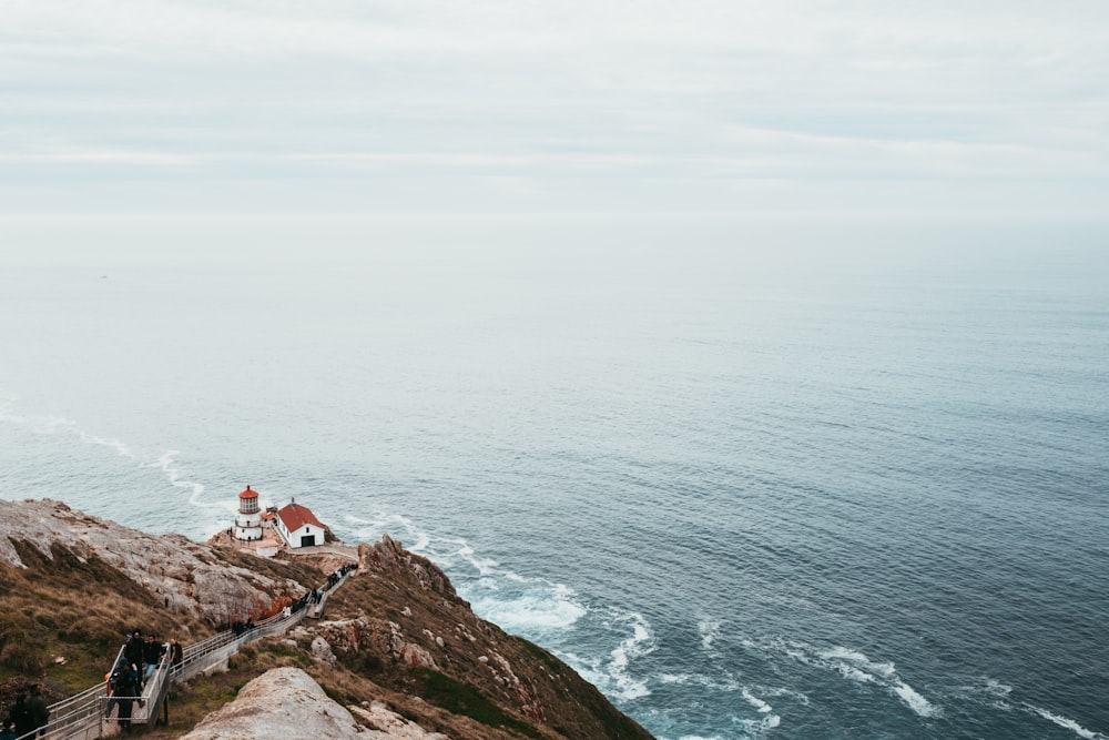 house and lighthouse near cliff and body of water aerial photography