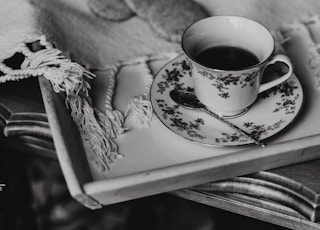 grayscale photography of teacup on a tray near cookies and jar