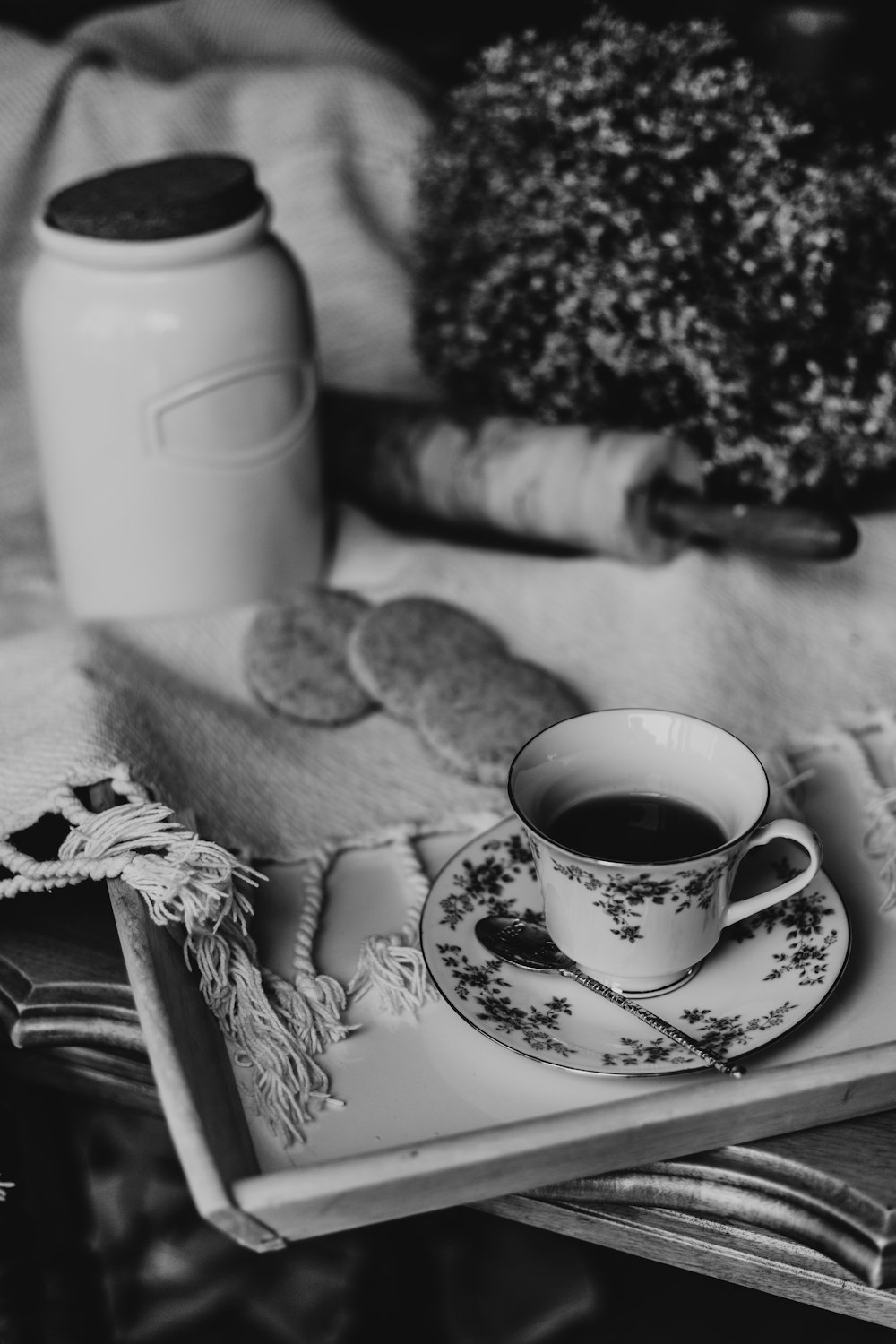 Graustufenfotografie einer Teetasse auf einem Tablett in der Nähe von Keksen und Glas