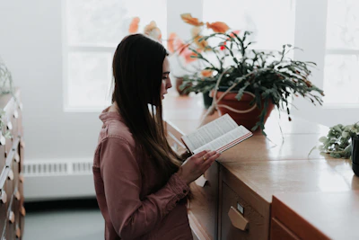 woman reading a book in front of brown wooden drawer