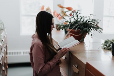 woman reading a book in front of brown wooden drawer