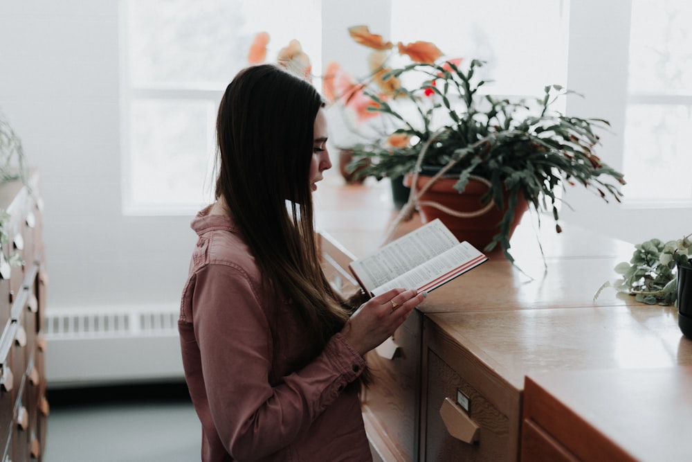 woman reading a book in front of brown wooden drawer