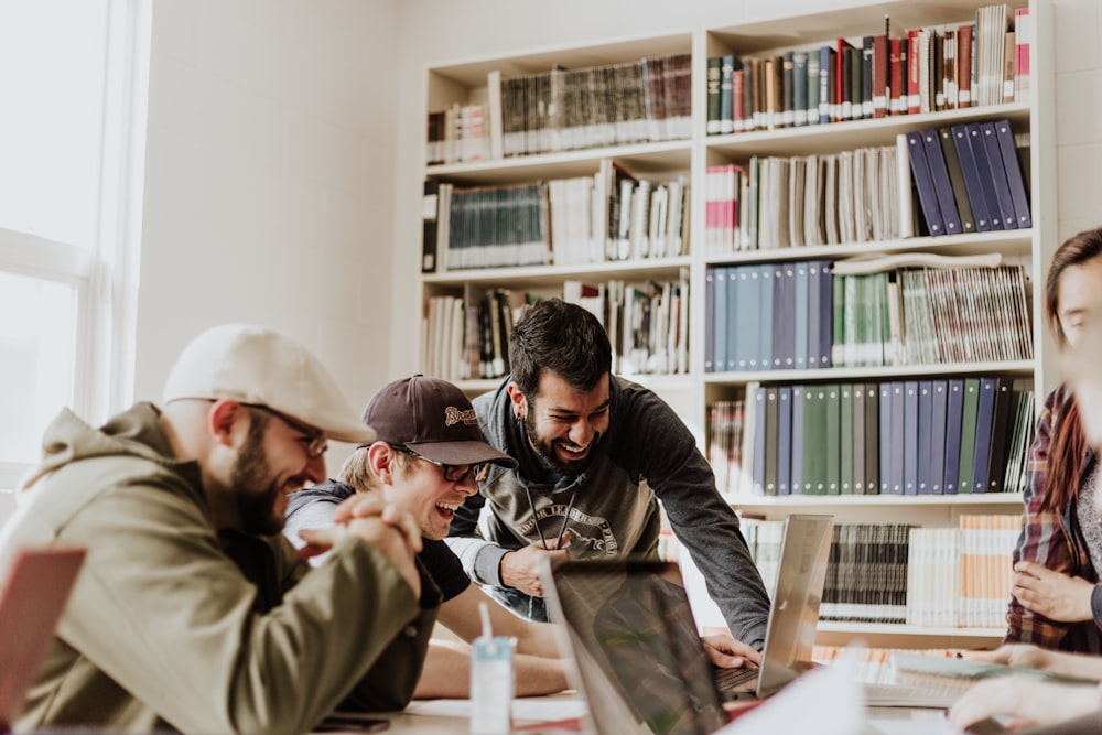 three men laughing while looking in the laptop inside room Unsplash