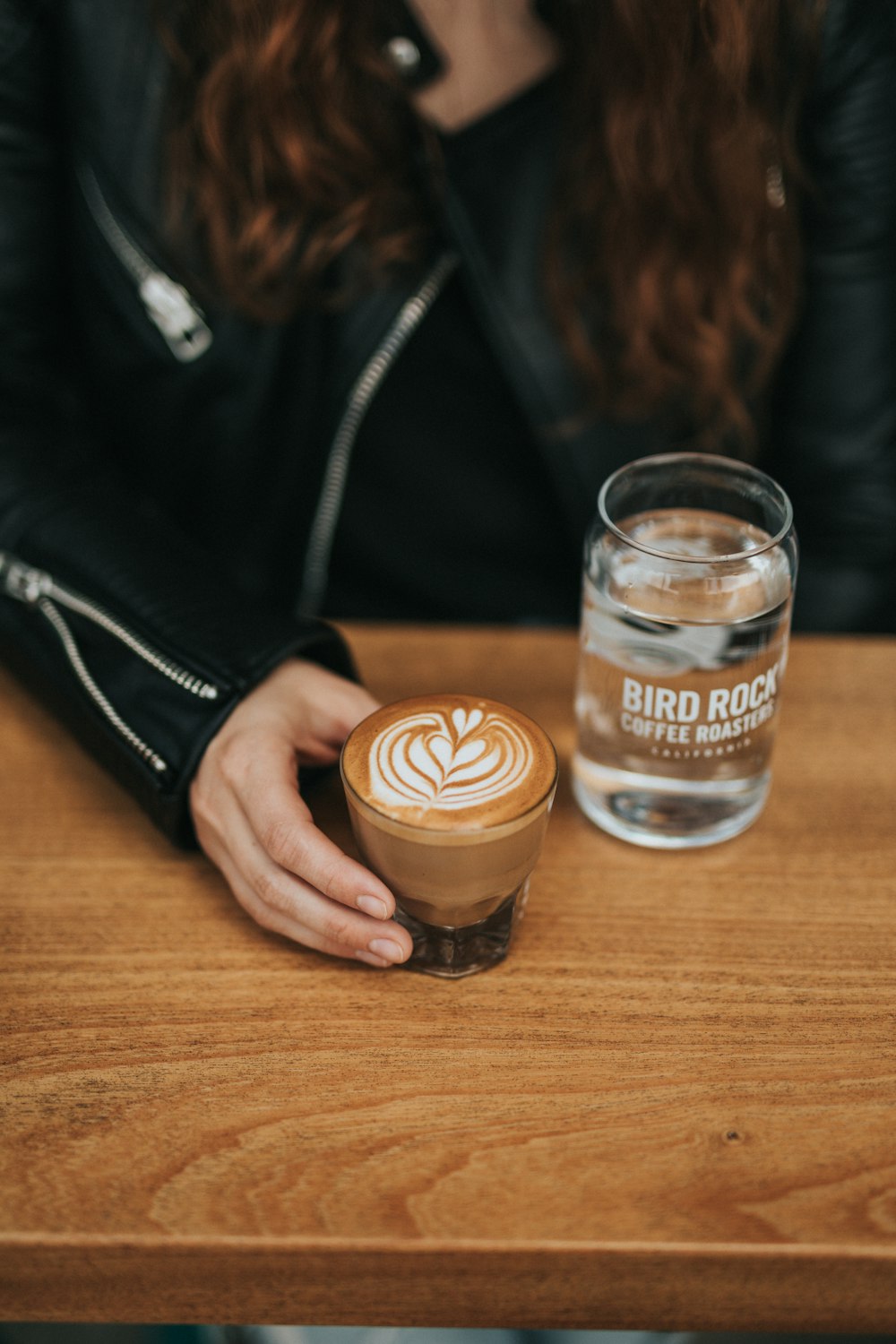 woman holding a glass of cappuccino beside glass of water on the table