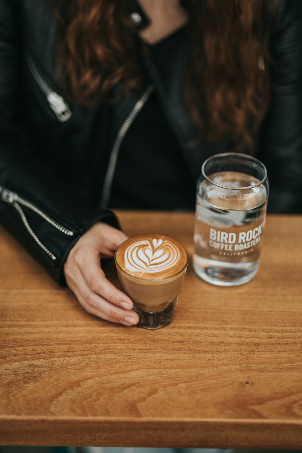 mulher segurando um copo de cappuccino ao lado de copo de água na mesa