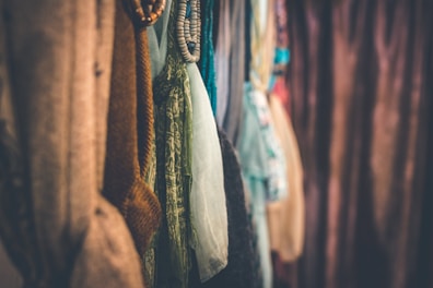 A row of colorful fabrics and textiles hangs closely together, showcasing various textures and patterns. Soft lighting adds a cozy and inviting atmosphere to the scene.