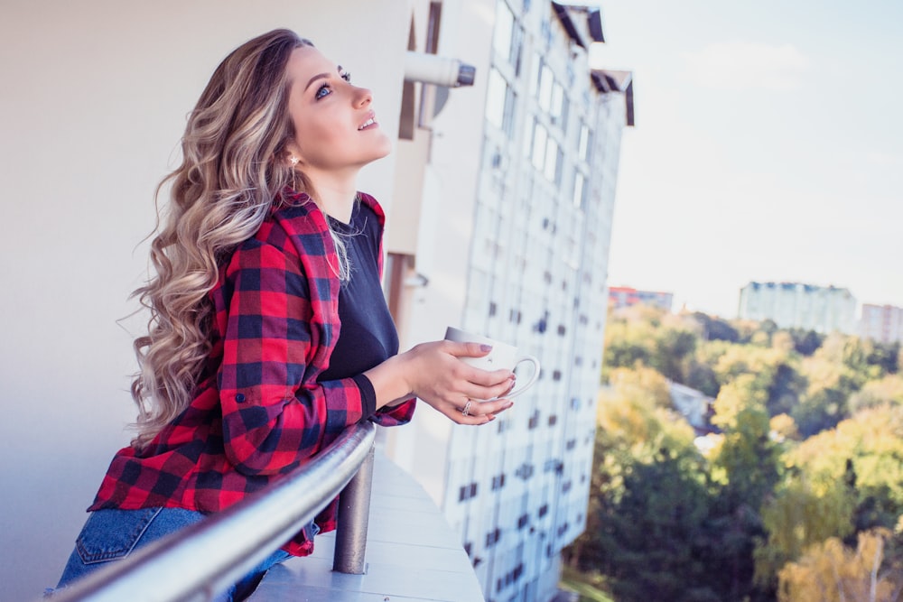 femme regardant vers le haut tout en s’appuyant sur le balcon d’un immeuble