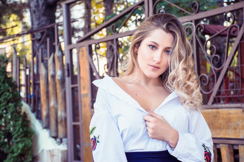 woman in white top standing beside brown metal fene