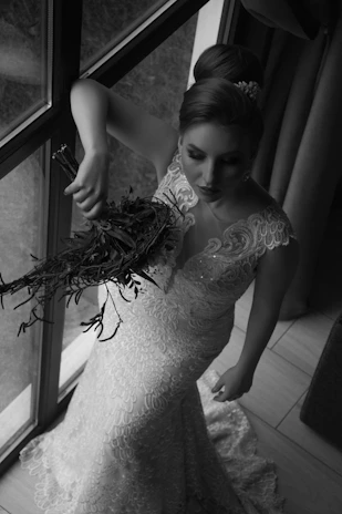 Model wearing an elegant lace dress from İda Laca, standing by a sunlit window.