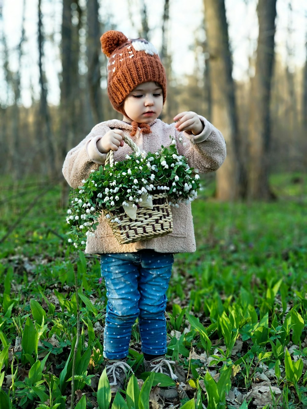 숲에서 꽃으로 가득 찬 바구니를 들고 있는 유아 소녀