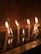 Several white candles are lit, casting a warm glow against a dark, reflective surface that appears to be water. The background features a tiled wall that absorbs the light, creating a serene and contemplative atmosphere. Some wax has dripped and congealed on the surface below, enhancing the sense of tranquility.