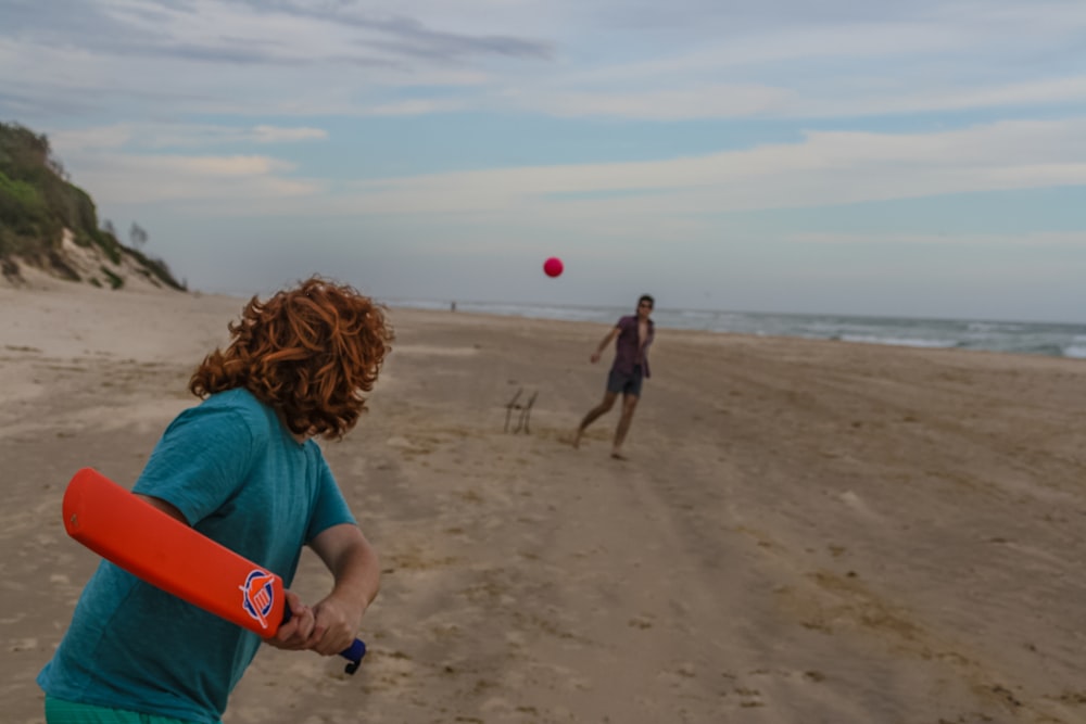 Persona sosteniendo un bate de cricket rojo cerca de la orilla del mar