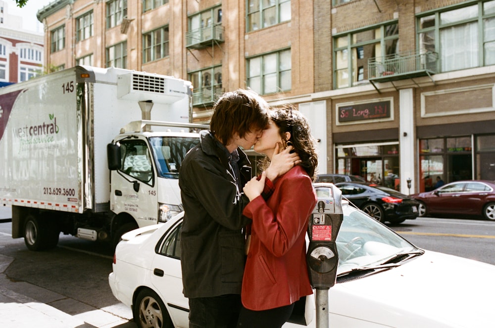 man kissing woman near white car