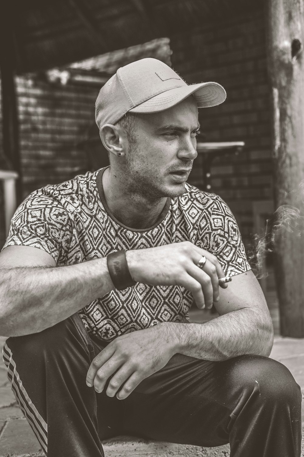 grayscale photo of man sitting on holding cigarette stick