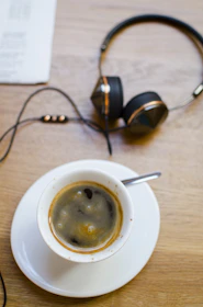 Close-up of headphones resting on a wooden table next to a steaming cup of tea.