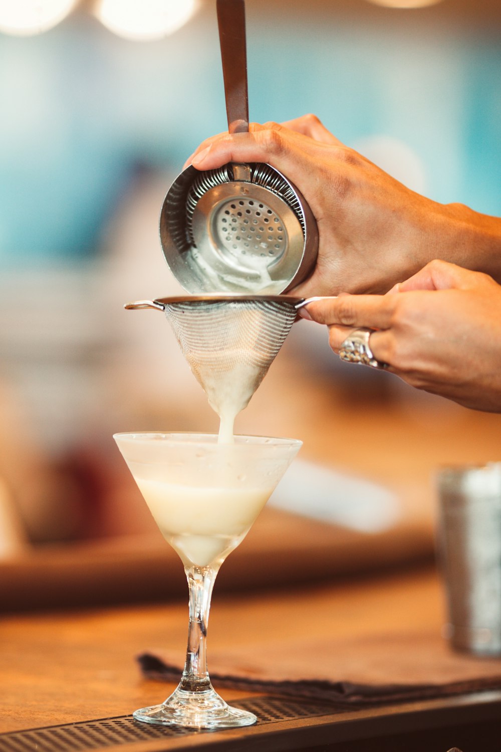 person holding container pouring white liquid on martini glass