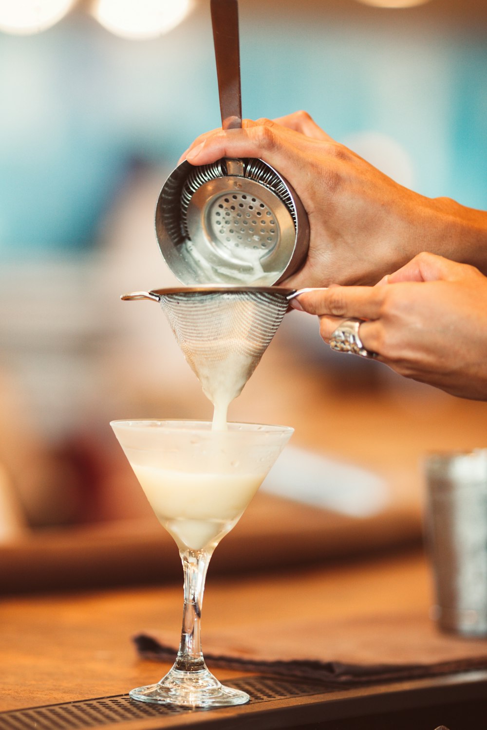 personne tenant un récipient versant un liquide blanc sur un verre à martini