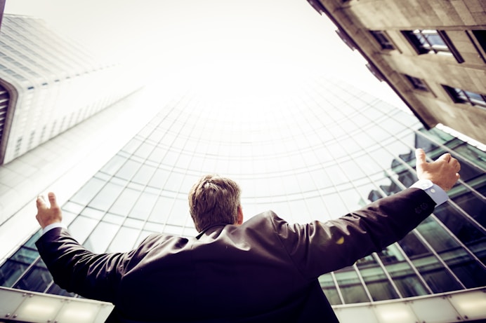 Man in suit raising arms towards a glass skyscraper, symbolizing professional growth and aspirations