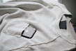 A dark smartphone is partly visible in the pocket of a light beige or off-white sweatshirt. The sweatshirt is laid out flat, with its seams and pocket details clearly visible.