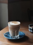 clear drinking glass filled with brown coffee on teal ceramic saucer