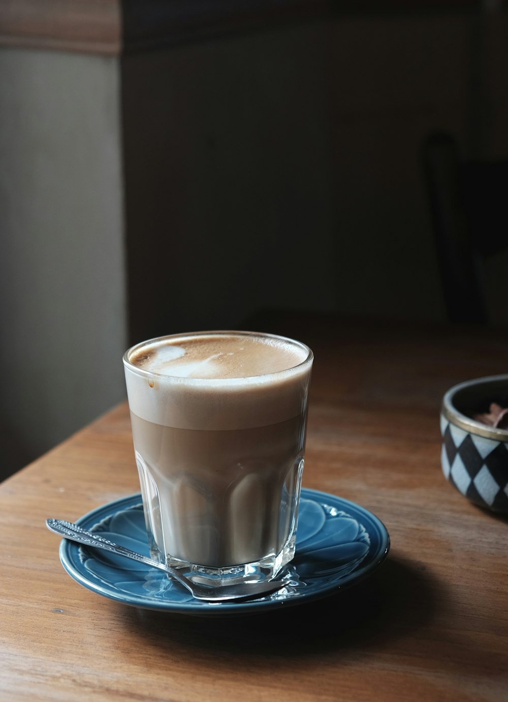 klares Trinkglas gefüllt mit braunem Kaffee auf blaugrüner Keramikuntertasse