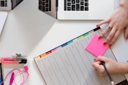 person holding pencil and stick note beside table