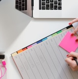 person holding pencil and stick note beside table