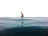 Woman sitting on a surfboard in calm water, looking towards the horizon with a peaceful expression.