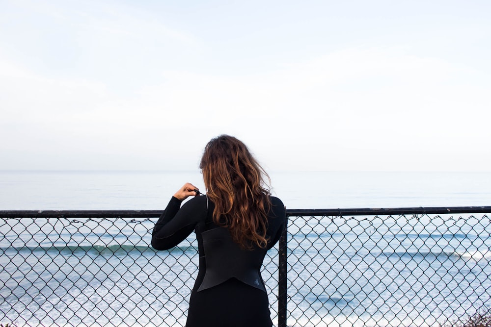 woman leaning on fence facing sea