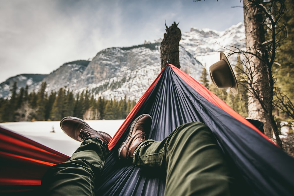 person lying on hammock near brown hat hanging on tree branch