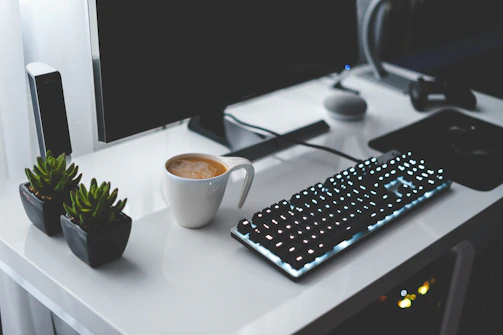 Un ordinateur à l'écran plat avec son clavier noir près d'une tasse de thé sur un bureau