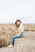laughing woman sitting on concrete surrounded by brown grass