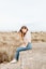 laughing woman sitting on concrete surrounded by brown grass