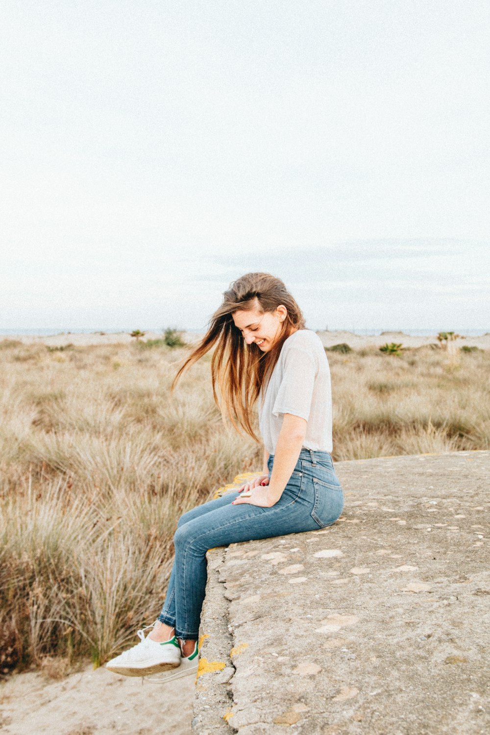 laughing woman sitting on concrete surrounded by brown grass