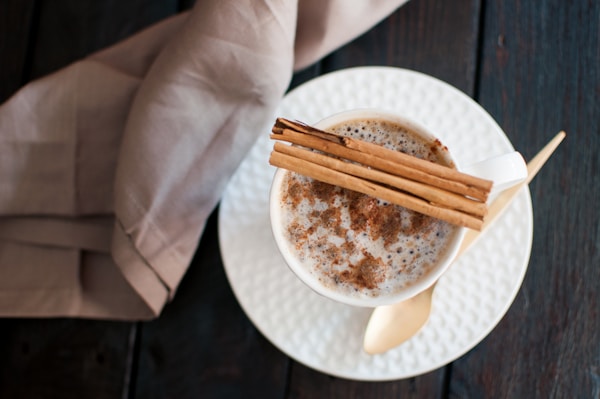 white ceramic mug on saucer beside beige plastic spoon