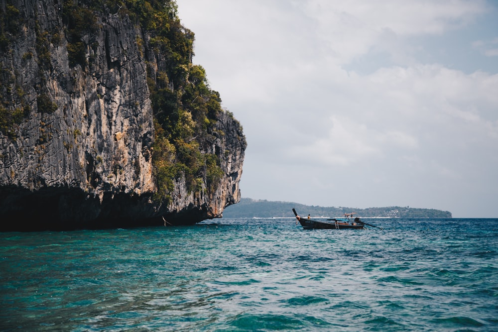 boat on body of water near brown rock formation during daytime