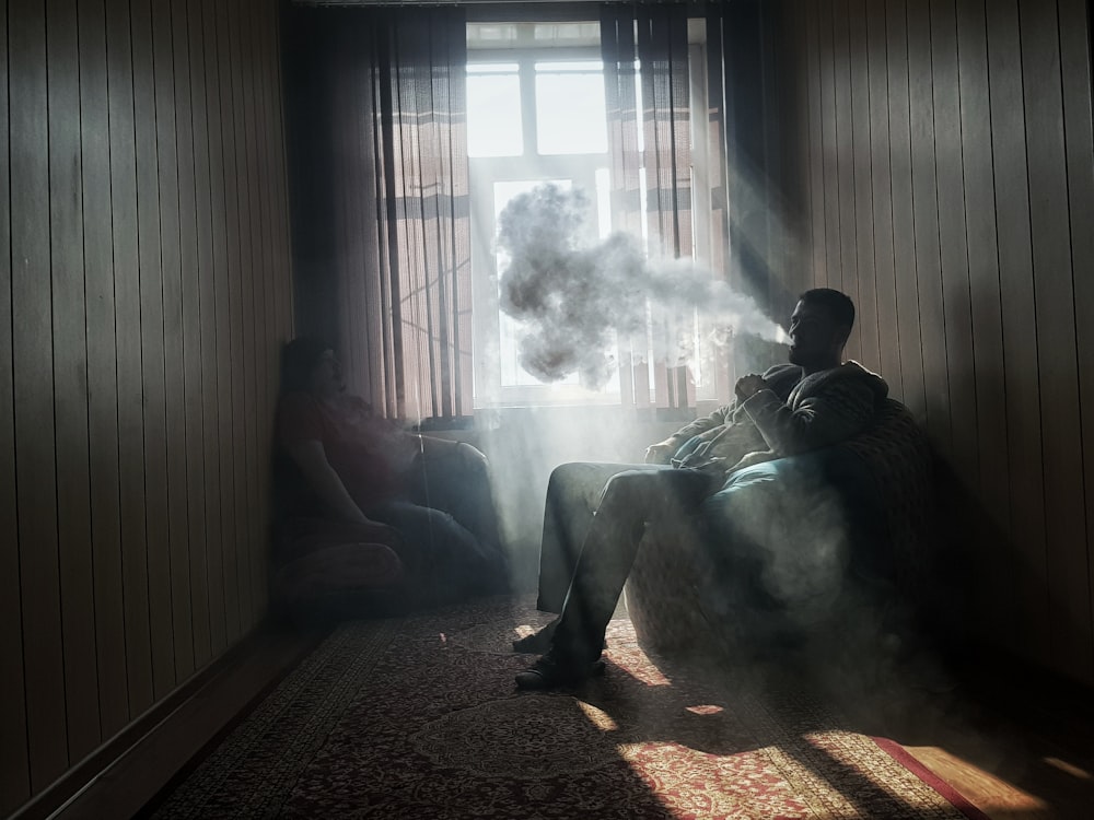 man sitting on armchair near window while smoking