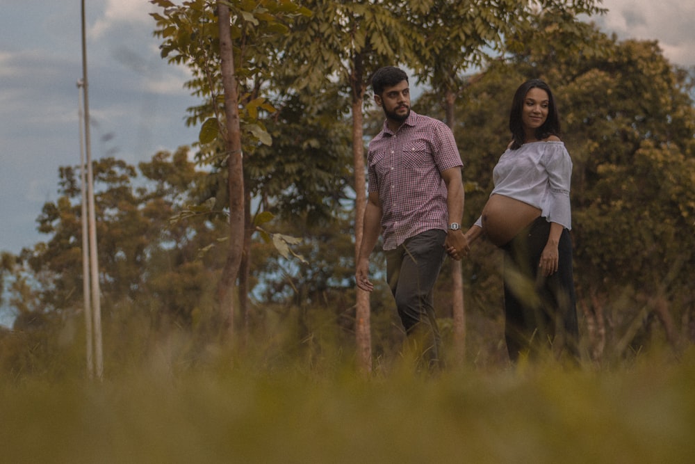 male and female holding hand while standing near tree