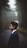 A person in a suit stands in profile on a foggy, forested road. Tall trees line the path, creating a serene yet mysterious atmosphere.