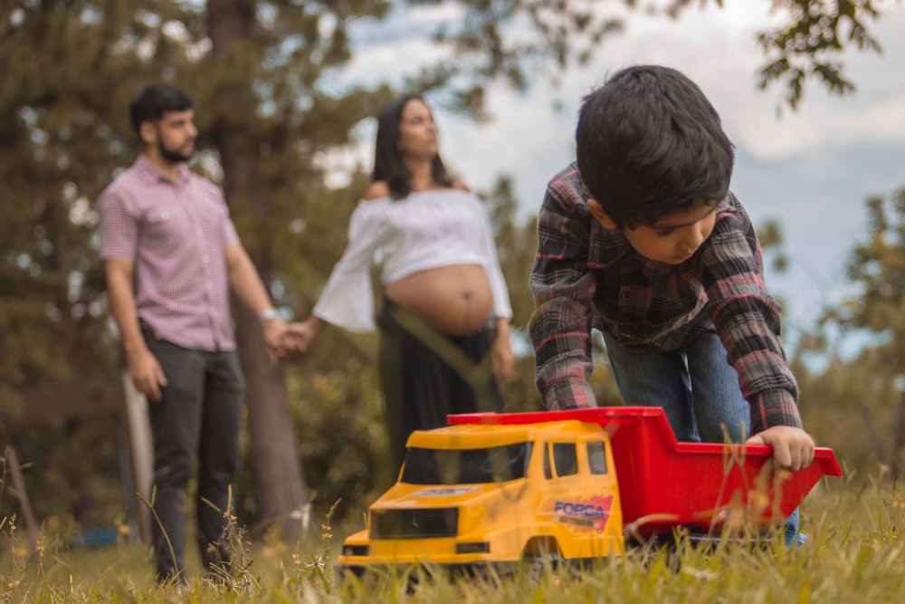 boy playing red and yellow truck on grass field