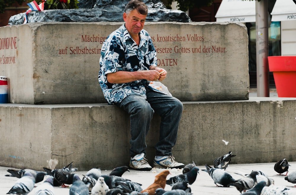 Mann sitzt auf dem Bürgersteig und füttert Tauben